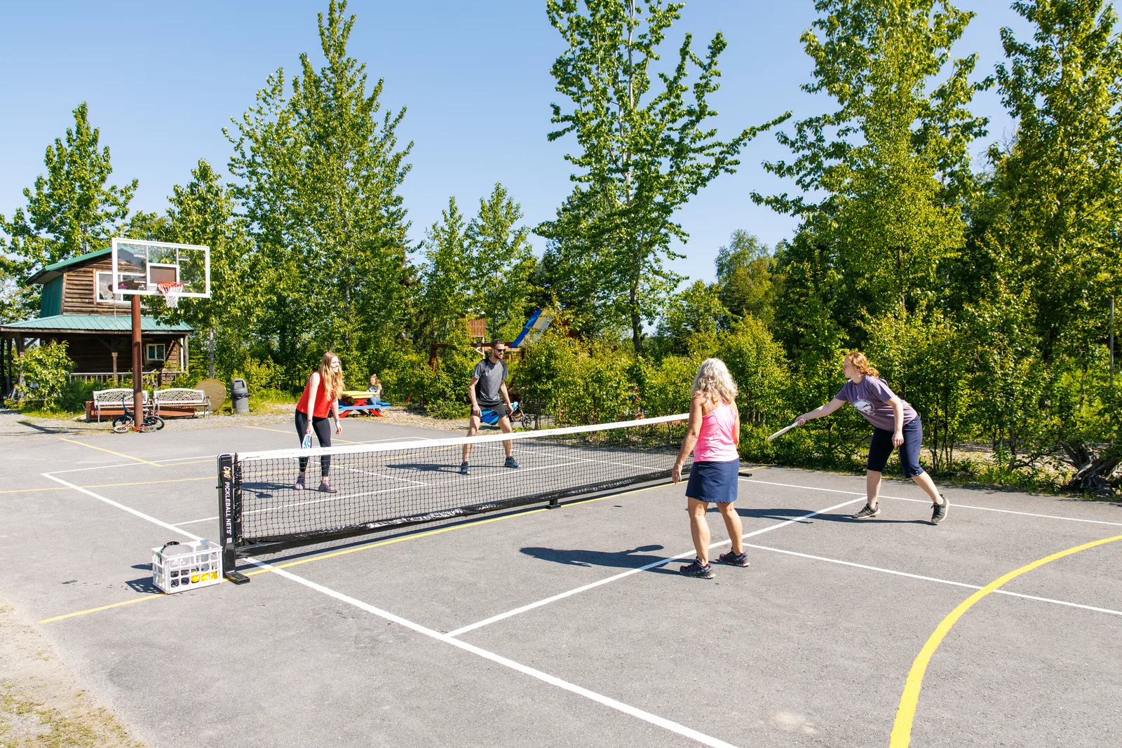 Guests playing pickleball on the outdoor court with a basketball hoop